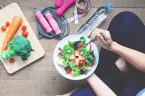 Overhead view of a person eating salad beside vegetables and a skipping rope