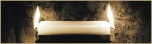 Two lit candles against a dark wall