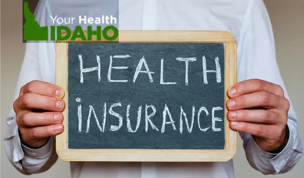 Person holding a chalkboard reading Health Insurance, from Your Health Idaho