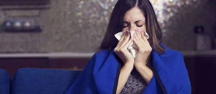 Woman in a blue coat blowing her nose
