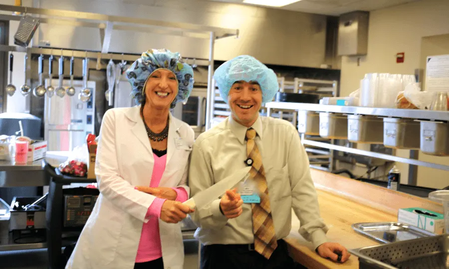 Two staff members in hairnets cutting a ribbon in the hospital kitchen