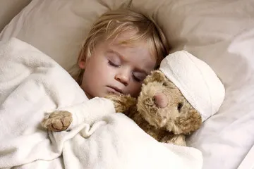 Toddler asleep in bed holding a teddy bear with a bandaged head