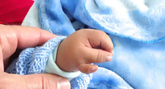 Newborn's hand and foot wrapped in a blue blanket