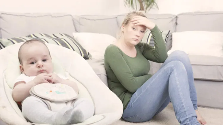 Mother looking exhausted on the floor beside her baby in a seat