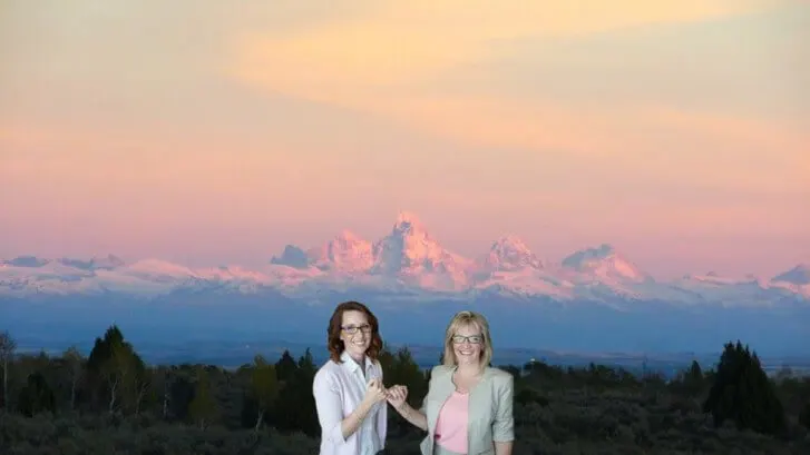 Two women standing in sagebrush with the Teton Range at sunset