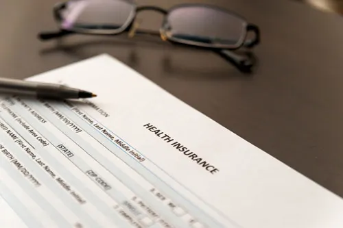 Health insurance paperwork with reading glasses and a pen