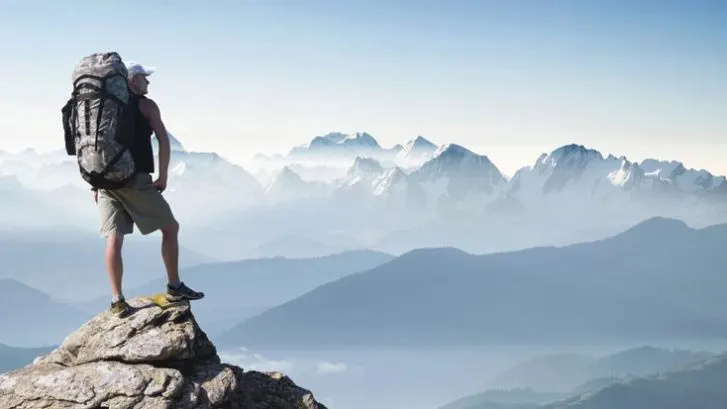 Hiker with a backpack standing on a summit looking over the mountains