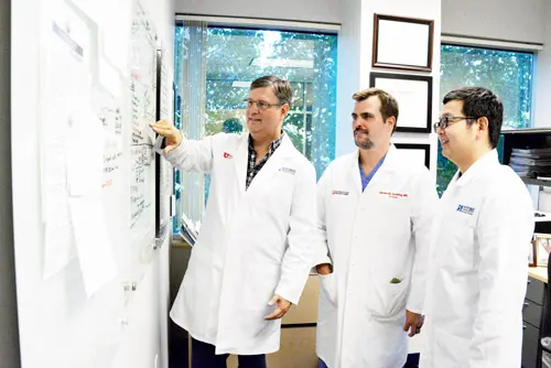 Three doctors in white coats discussing notes at a whiteboard