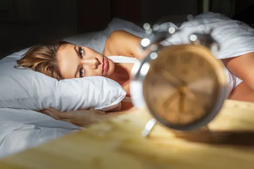Woman lying awake in bed beside an alarm clock