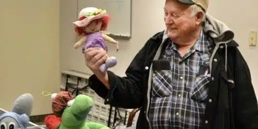 Man holding up a puppet at a community craft table