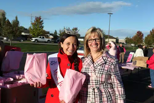 Two women at a pink-draped stall during an outdoor community event