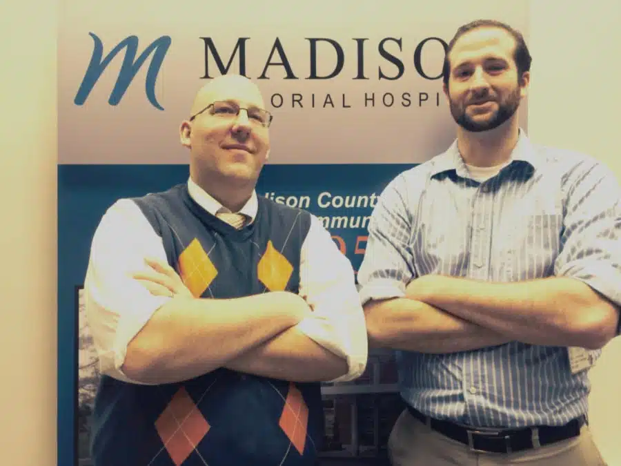 Two staff members with arms folded in front of a Madison Memorial banner