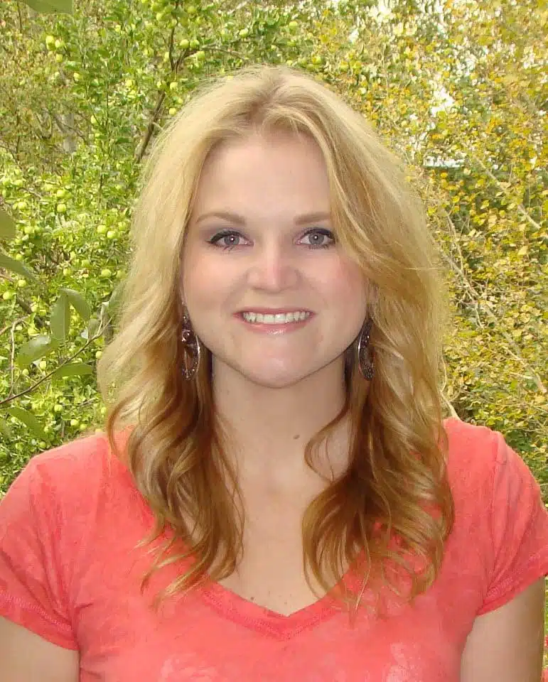 Madisonhealth staff portrait: woman in a coral top with autumn trees behind