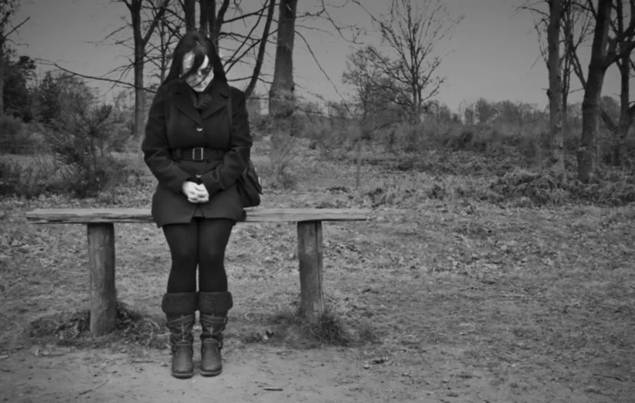 Black-and-white photo of a woman sitting alone on a bench in a bare winter park
