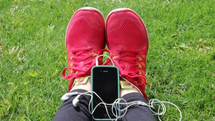 Red running shoes on grass beside a phone and earphones