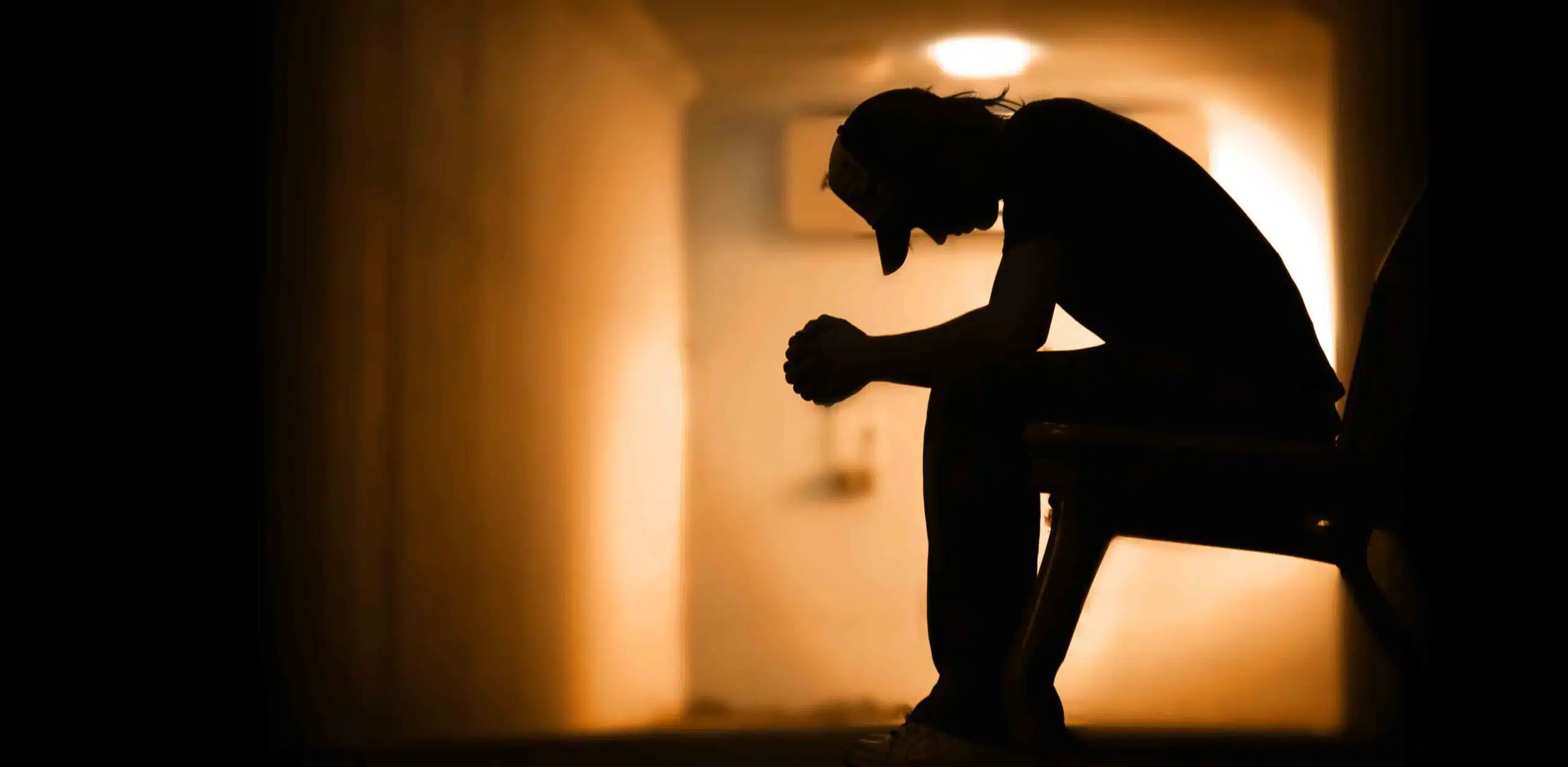 Silhouette of a person sitting hunched over in a dark corridor