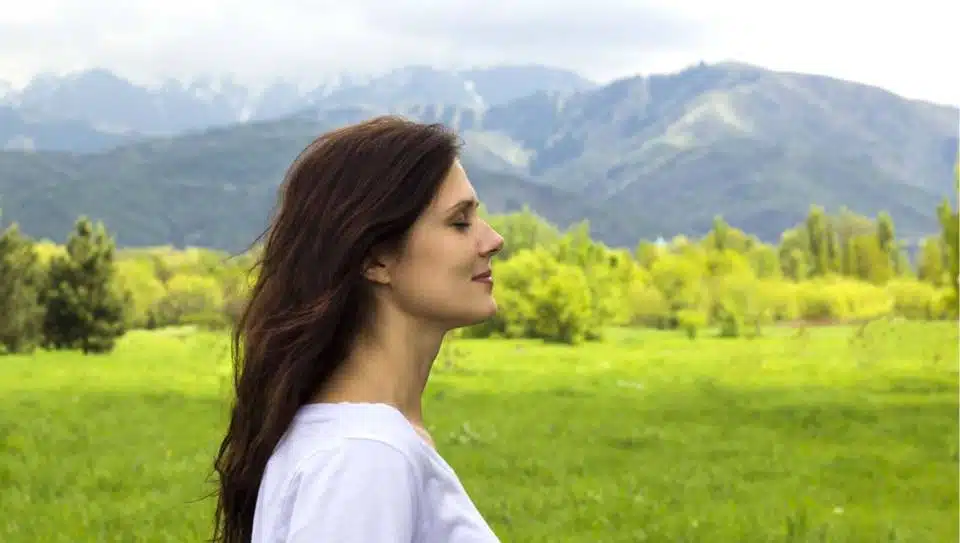 Woman standing in a green meadow with mountains behind her
