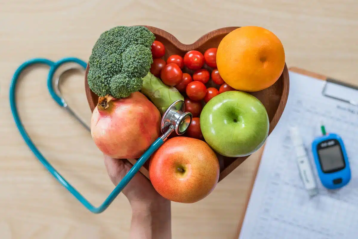 Heart-shaped bowl of fruit and vegetables with a stethoscope and glucose meter