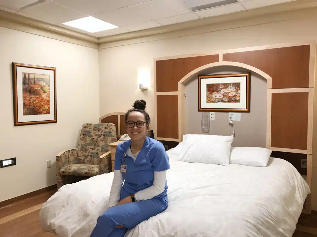 Nurse sitting on the bed in a hotel-style patient room