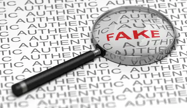 Magnifying glass revealing the word FAKE among repeated "authentic" text
