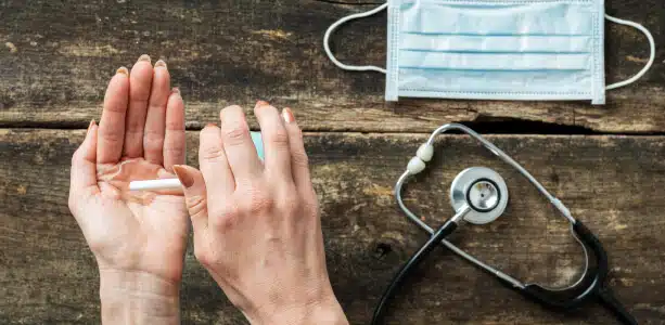 Open hands beside a face mask and a stethoscope on a wooden table