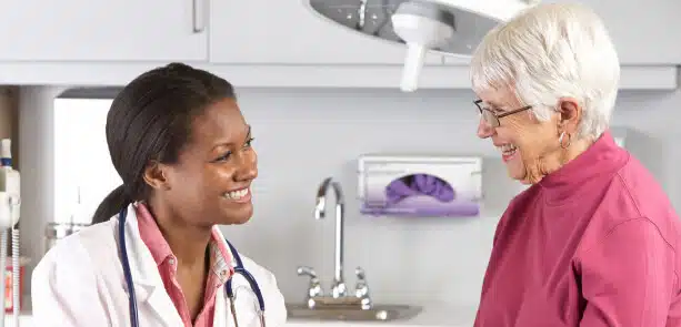 Doctor in a white coat talking with an older woman in an exam room