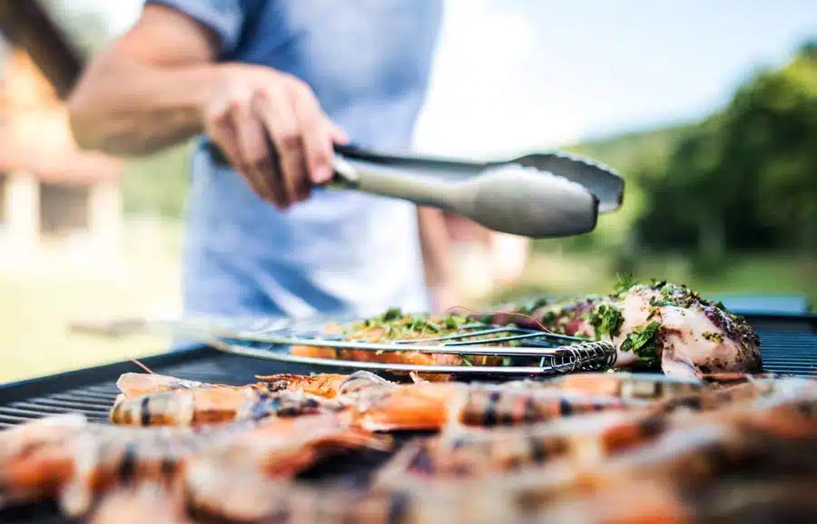 Person turning chicken and prawns on a barbecue with tongs