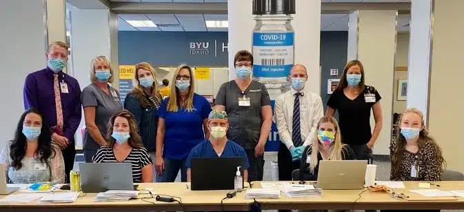Masked staff gathered around a table in a hospital meeting room