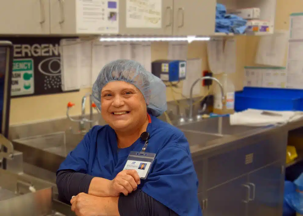 Staff member in a surgical cap and blue scrubs in a sterile processing room