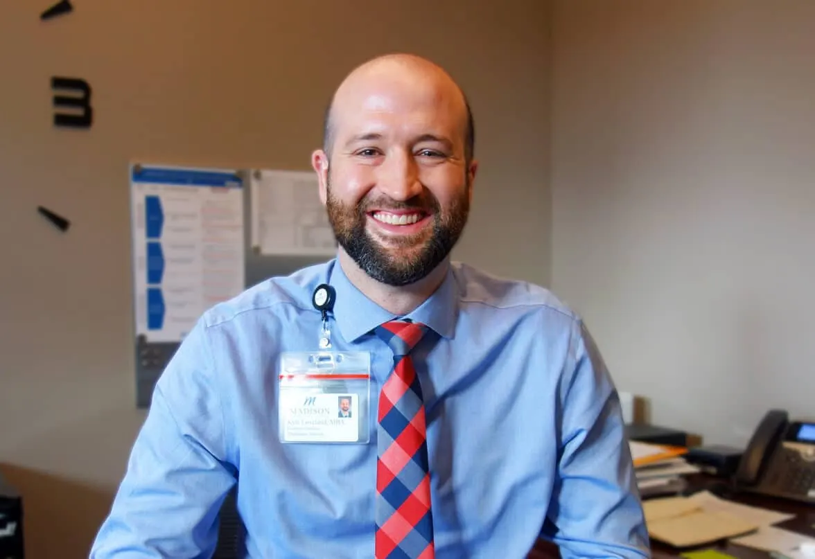 Madisonhealth staff member in a shirt and tie smiling at his desk