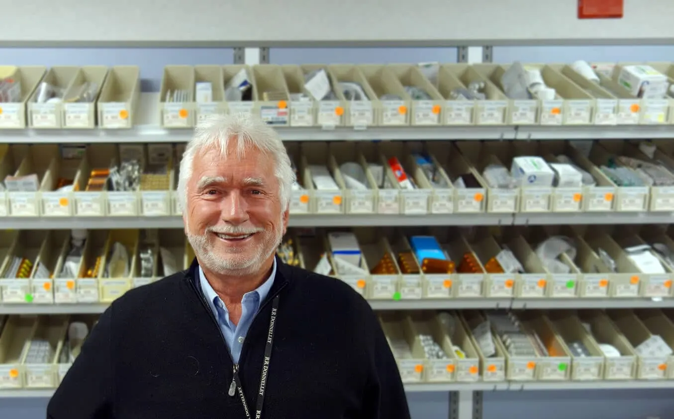 Pharmacy staff member smiling in front of the medication shelves