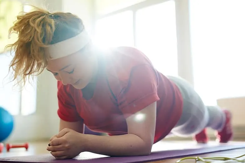 Woman holding a plank position on an exercise mat at home