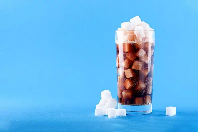 Glass of cola filled with sugar cubes on a blue background
