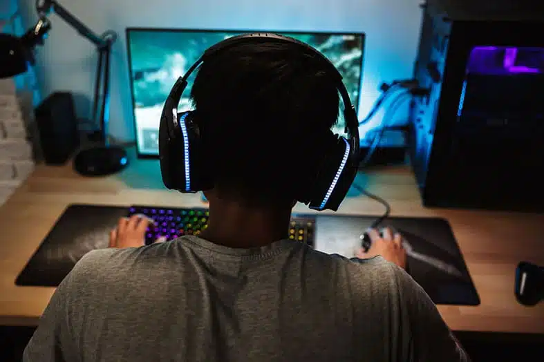 Person wearing headphones gaming at a computer late at night