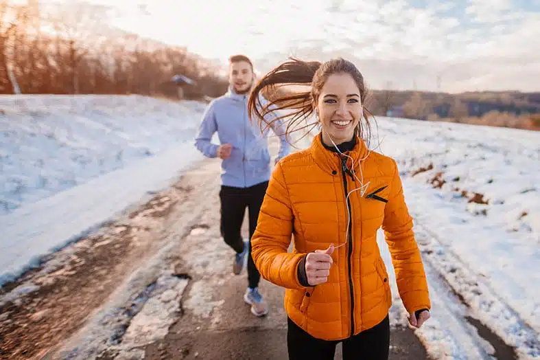 Two runners jogging along a snowy road in winter