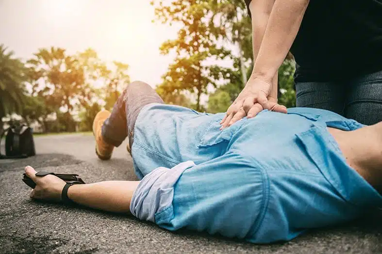 Bystander performing chest compressions on a man collapsed outdoors