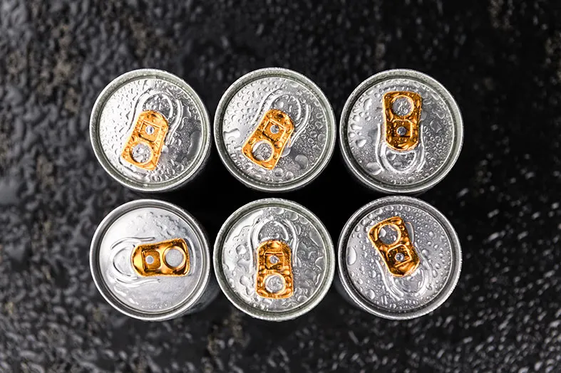 Six soda cans seen from above on wet asphalt