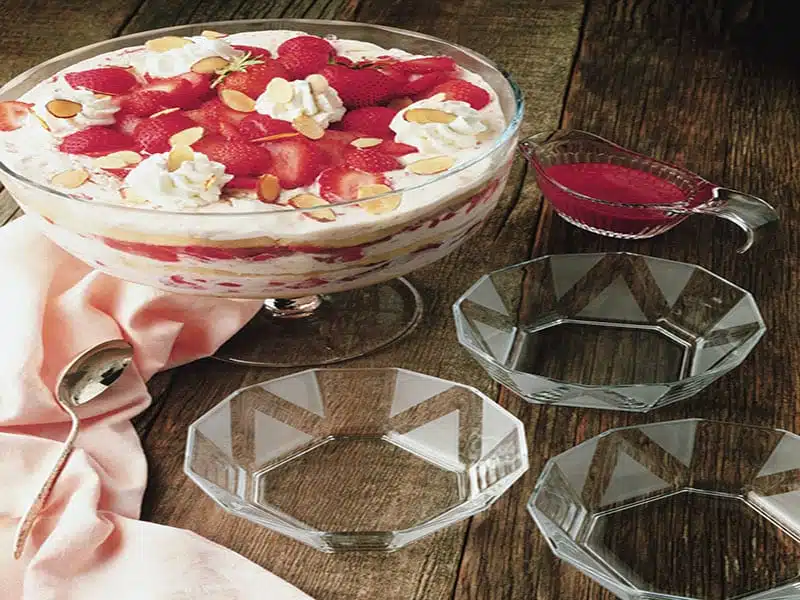 Strawberry trifle in a glass bowl beside empty dessert plates