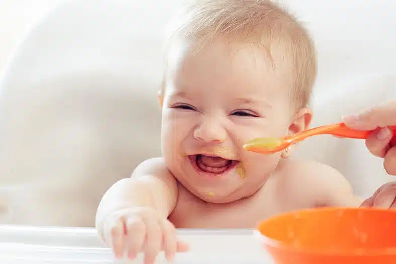 Laughing baby being spoon-fed puree