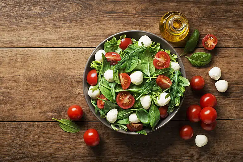 Bowl of spinach, tomato and mozzarella salad with olive oil and basil