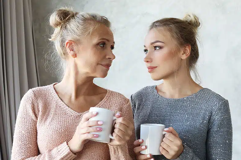 Mother and adult daughter talking over mugs of tea