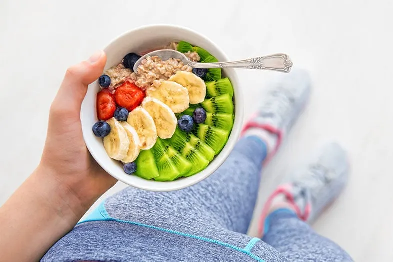 Person holding a bowl of oatmeal topped with berries, banana and kiwi