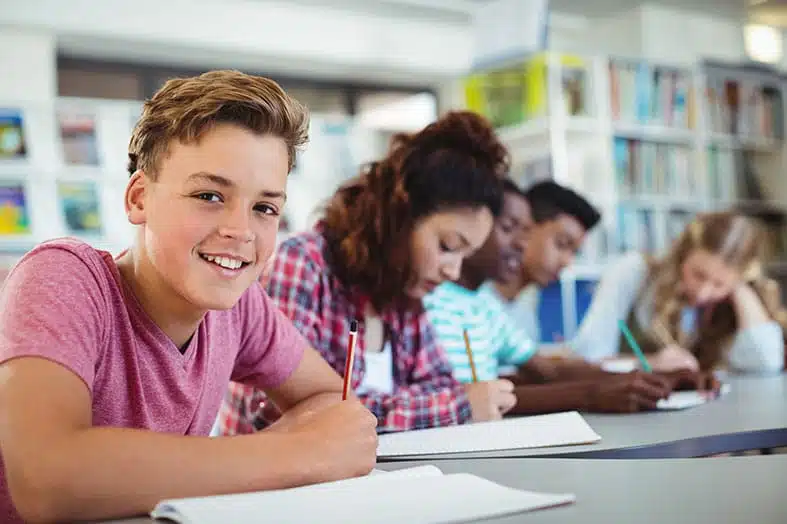 Teenage students writing at a table in a school library