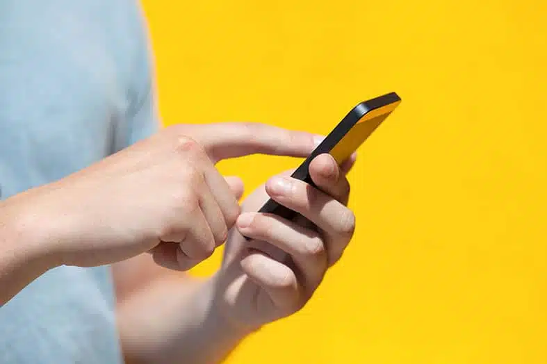 Person tapping on a smartphone against a yellow background