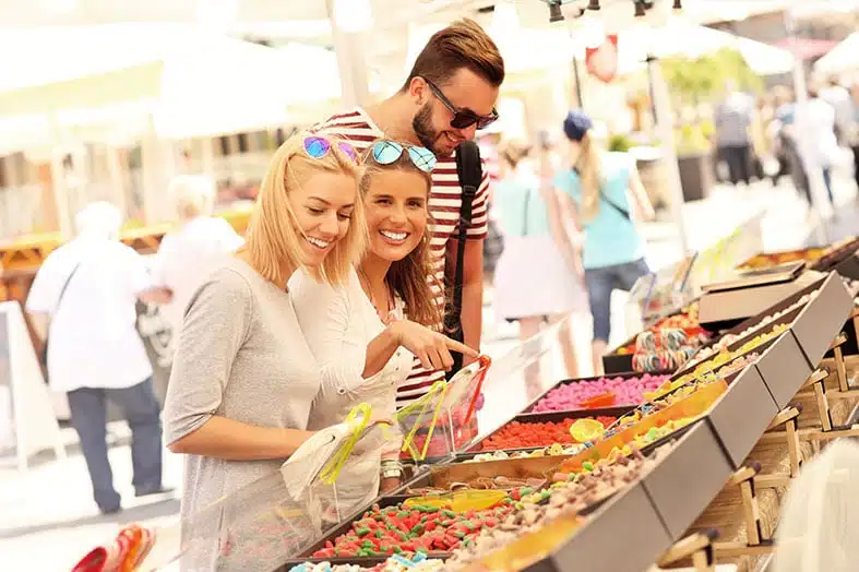 Friends browsing a market stall of sweets on a sunny street