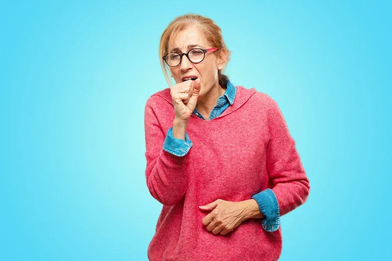 Woman in a pink sweater coughing into her fist