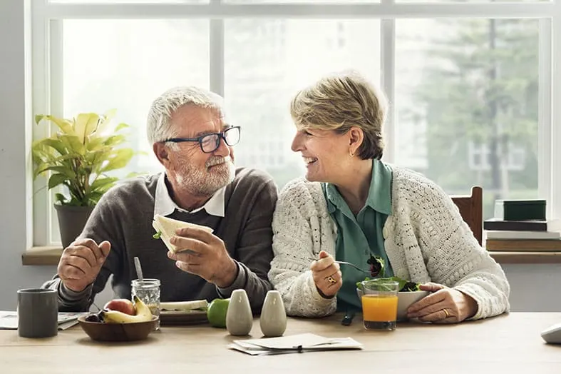 Older couple eating breakfast together beside a window
