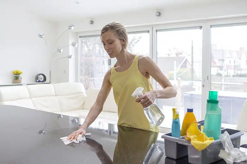 Woman wiping down a glass table with cleaning supplies beside her