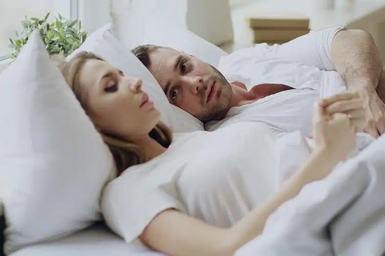 Couple in bed, one asleep and the other lying awake