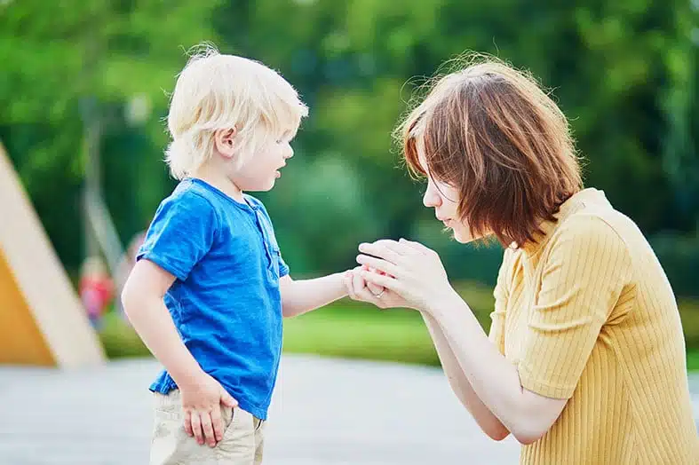 Mother crouching to talk with her young son outdoors